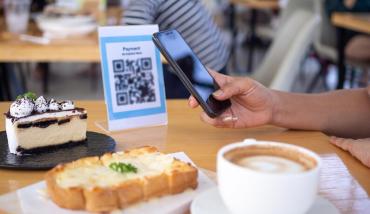 Una mujer paga en una cafetería usando el código QR interoperable de MODO hacia una terminal PayWay de LAPOS de la Mutual del Club Atlético Pilar